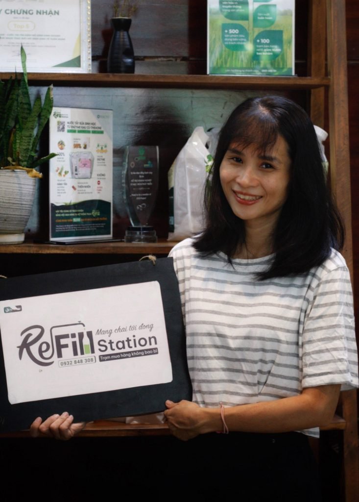 Người phụ nữ mỉm cười cầm túi vải ReFill Station - Trạm mua hàng không bao bì.
